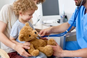 A young boy with his teddy bear being checked