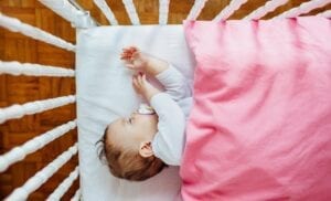 A baby sleeping in a crib and pink blanket