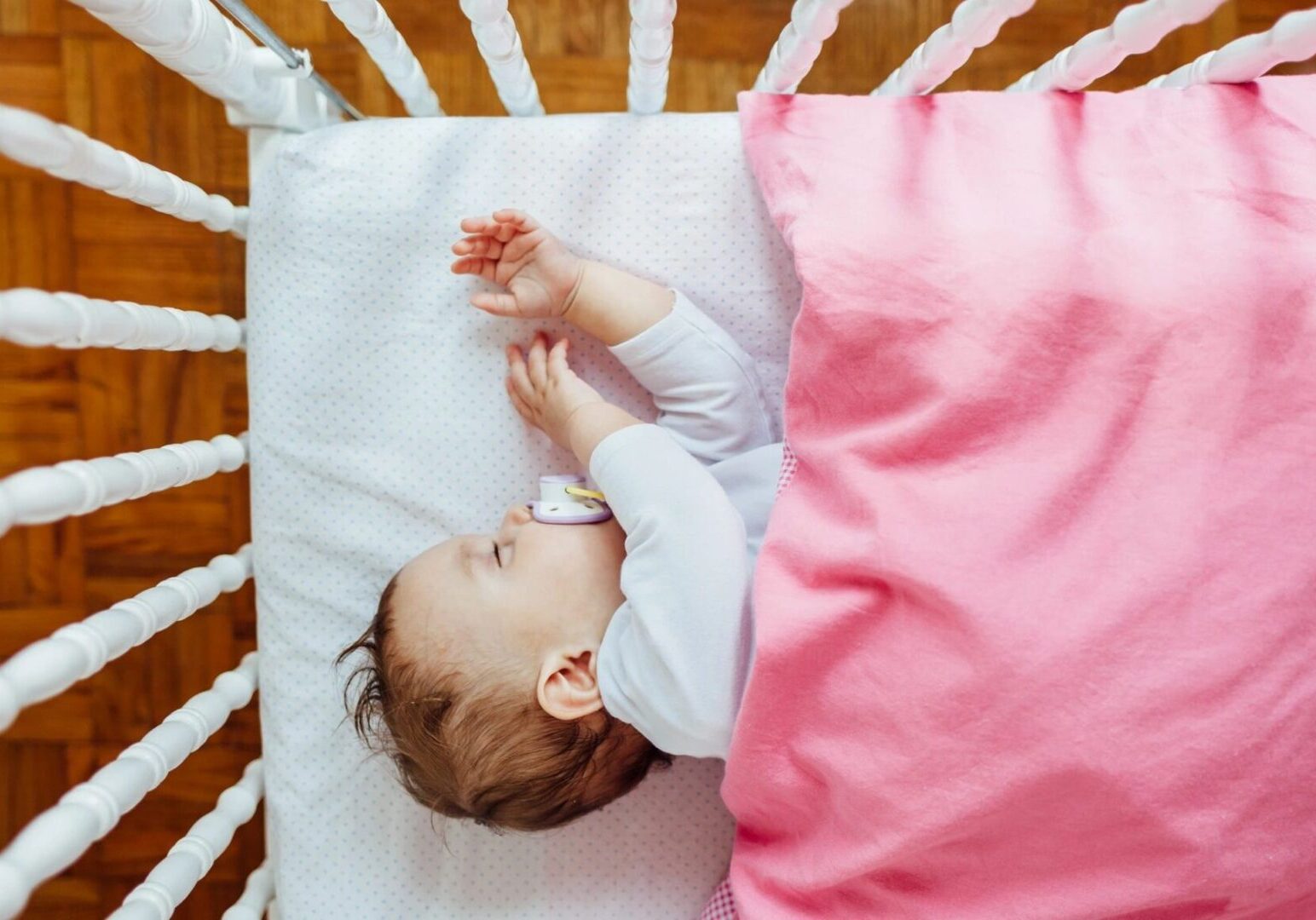 A baby sleeping in a crib and pink blanket